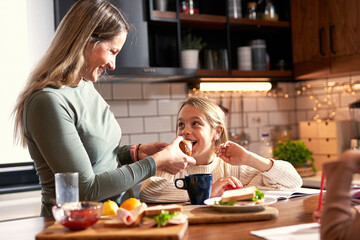 A little girl, pencil in hand, works on homework as her mother assists, blending breakfast and learning into a delightful morning routine.