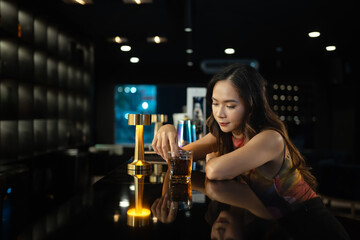 Elegant young woman with glass of whiskey sitting alone at bar counter