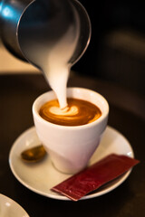 Milk pitcher pouring cream into a coffee cup. Vertical
