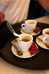 Waiter pouring milk into the coffee cup before serving it to the table. Vertical