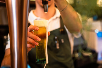 Unrecognizable bartender pouring beer at the restaurant with the foam falling off