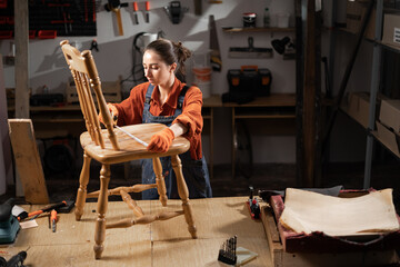 Young woman restorer of old wooden furniture measures the seat of a chair with a measuring tape, concept of renovation and restoration of old furniture