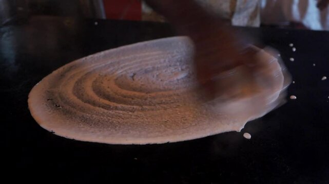 indian street food vender making dosa on hot pan
