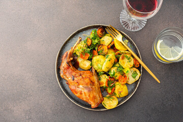 A hearty delicious dinner, baked rabbit with potatoes and carrots, a set table with food, a glass of wine and a vase of flowers