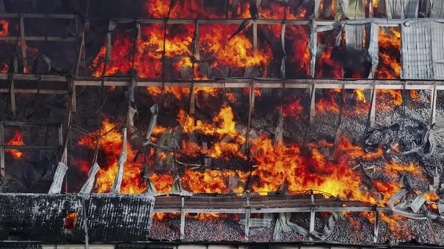Glowing fire on industrial warehouse. Destroyed building with orange flames. Burning house in city at sunny day. Aerial top down shot.