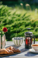 French press with coffee and croissants on a patio table