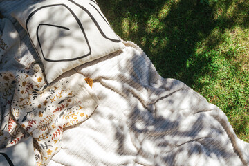 White blanket and pillows on grass in the shade of a tree