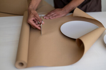 Hands cutting brown wrapping paper to pack plates, close-up view.