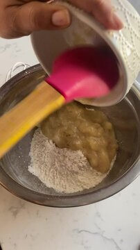 Vertical video of mashed bananas into a bowl of flour making banana donuts