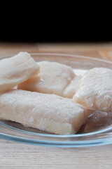 Frozen haddock fillets defrosting on a glass plate. On a wooden chopping board background