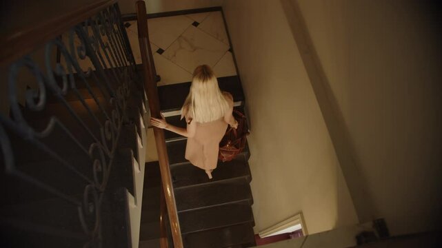 blonde girl in a long dress with a travel bag climbing the stairs, top view