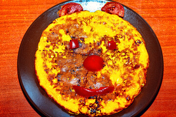  Plate with a smiling face created on it.  Plate of food with a face drawn on it, for children breakfast. The face has a smile and is made up of a yellow omelet, tomatoes, and peppers