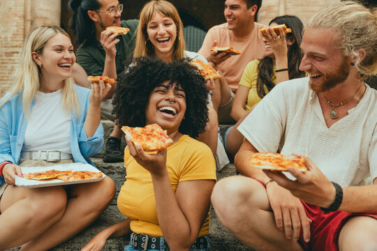 Fototapeta Multicultural smiling friends eating pizza sitting outside - Cheerful young people enjoying summer vacation together - Happy life style concept with guys and girls hanging out on a sunny day