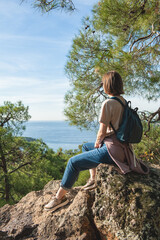 Naklejka premium Woman with a backpack looking out at a scenic view of hills and trees, sitting on a rock