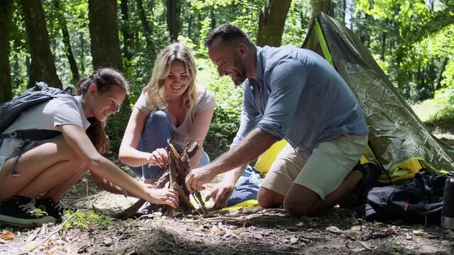 Family backpackers set up a campfire together in nature on a sunny summer day, working as a team to prepare their campsite.