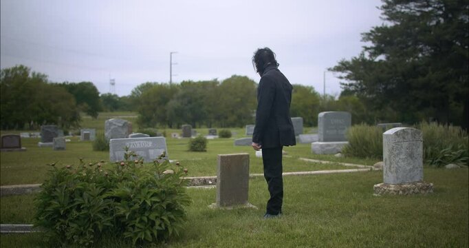 Man in black suit in cemetery for funeral ceremony.