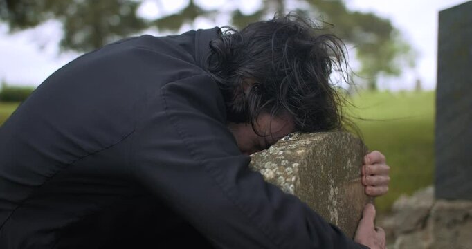 Sad, crying man grieving over grave in cemetery.