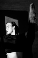 A young girl does stretching on a sports mat. Shot from above. Close-up portrait. Gymnastics and yoga classes in the studio. Black and white artistic vertical photo