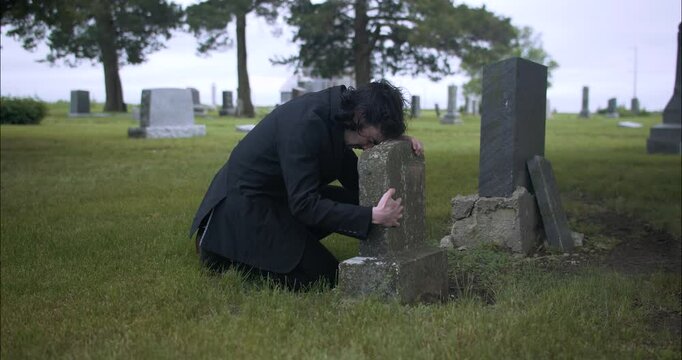 Man crying over grave, grieving death of loved one.