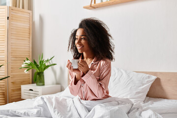 A curly African American woman in pajamas sitting on a bed, enjoying a cup of coffee in the morning sunlight.