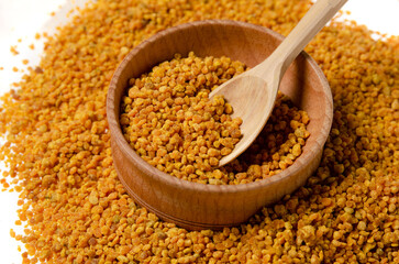 Bee pollen grains in spoon and pile isolated on white background