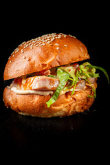Close-up of a fresh burger with sesame bun, lettuce, tuna and sauce on a dark background