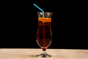 Glass of iced tea with lemon slices and a blue straw on a wooden table against a black background