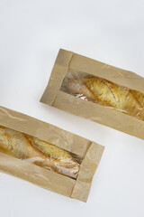 Closeup of two french baguettes in the brown kraft paper plastic bag isolated on white background. Fresh baked bread for sell. High resolution studio photo. Minimalist design. Top view. Copy space.