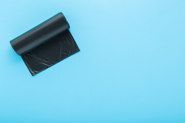 New dark black roll of plastic garbage bag on light blue table background. Pastel color. Closeup....