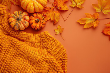 Fototapeta premium Autumn concept with warm orange sweater and pumpkins surrounded by colorful leaves on orange background with copy space