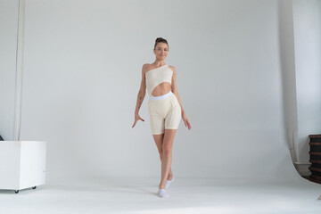 Obraz premium Woman in a stylish beige outfit, executing a dance move with precision and elegance in a bright studio. Concept: Showcasing the integration of fashion and fitness, encouraging an active and stylish