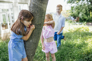 Little kids play hide-and-seek outdoors in garden. Summer fun in park.