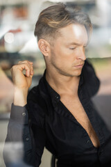 Fototapeta premium A handsome blonde man in stylish attire is captured in reflection of window
