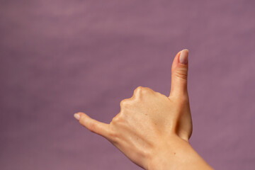 Beautiful female hand on isolated on purple background nude manicure hand showing symbol drink sign language call me