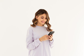 Happy pretty young woman model holding smartphone looking at cell texting message, smiling girl using mobile apps on cell phone standing isolated on white background with cellphone.