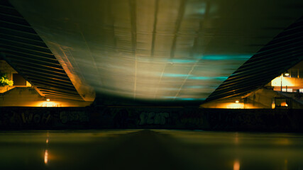 A low-angle view of an urban bridge at night, illuminated by city lights. The scene captures the industrial design and atmospheric lighting of the urban environment.