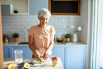 Senior woman preparing a healthy smoothie with fresh fruits in the kitchen