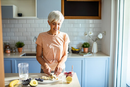 Senior woman preparing a healthy smoothie with fresh fruits in the kitchen