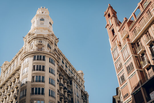 Upward view of a tall historic building with ornate details and numerous balconies in Valencia. The perspective emphasizes the city architectural elegance and grandeur.