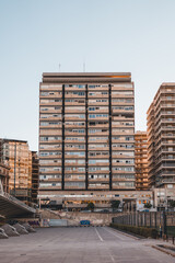 Tall urban residential building with balconies, surrounded by other high-rise structures in a cityscape. Suitable for real estate, urban development, and architecture themes.