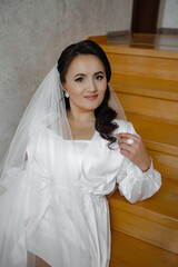 A woman in a white dress is posing for a picture on a staircase. She is wearing a veil and a ring...