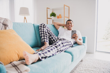 Photo of cheerful positive guy sleepwear pajama staying home sofa typing modern device indoors...