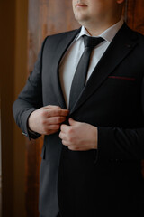 A man in a suit is getting ready to tie his tie. He is wearing a black suit and a white shirt