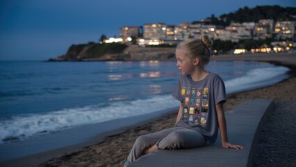 Fototapeta premium A young girl sitting on a concrete ledge overlooking the ocean, AI