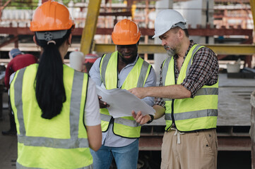Multi-ethnic workers wearing hard hats in Engineering Workshop. Three industrial workers in hard hats are conversing on the storeroom floor.