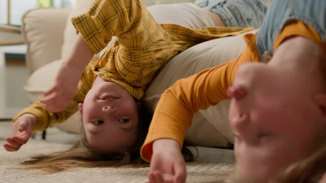 Happy playful family Caucasian kids little girls sisters children lying upside down couch having fun naughty daughters grimacing show tongue fooling around joking smile together friends home apartment