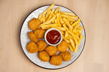 Top view of a plate of crispy fried chicken with French fries and a side of ketchup on wooden table