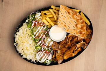 Delicious plate of mixed doner kebab with salad, fries, pita bread, and sauce on a wooden table