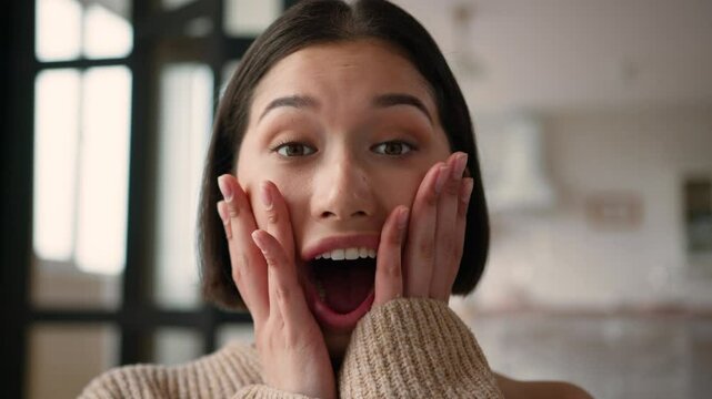 Portrait close up shocked Caucasian hispanic latin woman girl happy reaction shock emotion open mouth hold face excited female winner wonder amazing unexpected good news win surprise rejoice at home
