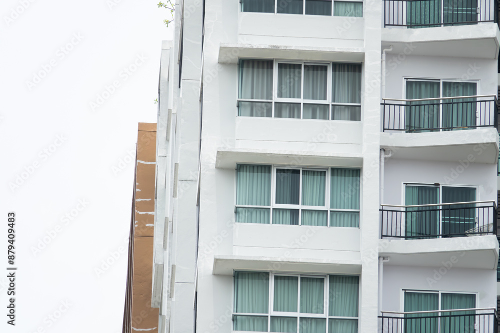 Wall mural A tall building with a lot of windows and a balcony. The building is white and has a brown section on the side